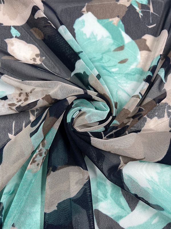 Close-up of the Printed Mesh - Lilly - 145cm by Super Cheap Fabrics, showcasing a floral fabric with a large leaves and flowers pattern in shades of turquoise, teal, beige, and black. The soft, semi-transparent mesh is gathered into a swirl at the center, highlighting the overlapping colors and textures.