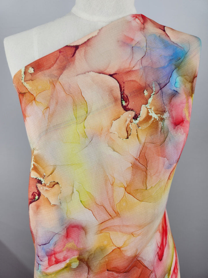 A mannequin is adorned with a piece of designer cotton from Super Cheap Fabrics called Aurelia. This fabric showcases a vivid watercolor pattern with swirls of red, yellow, blue, and pink hues that blend seamlessly together. It’s ideal for high-end sewing projects that require an artistic and lively visual texture.