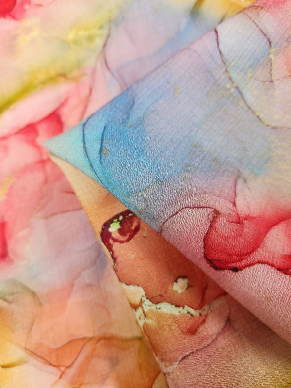 A detailed view of the Designer Cotton - Aurelia - 150cm by Super Cheap Fabrics reveals a vibrant, multicolored fabric with a watercolor-like pattern. This breathable material showcases soft blends of pink, blue, red, and yellow hues, forming an abstract and artistic design. With its smooth and lightweight texture, it is ideal for luxury sewing projects.