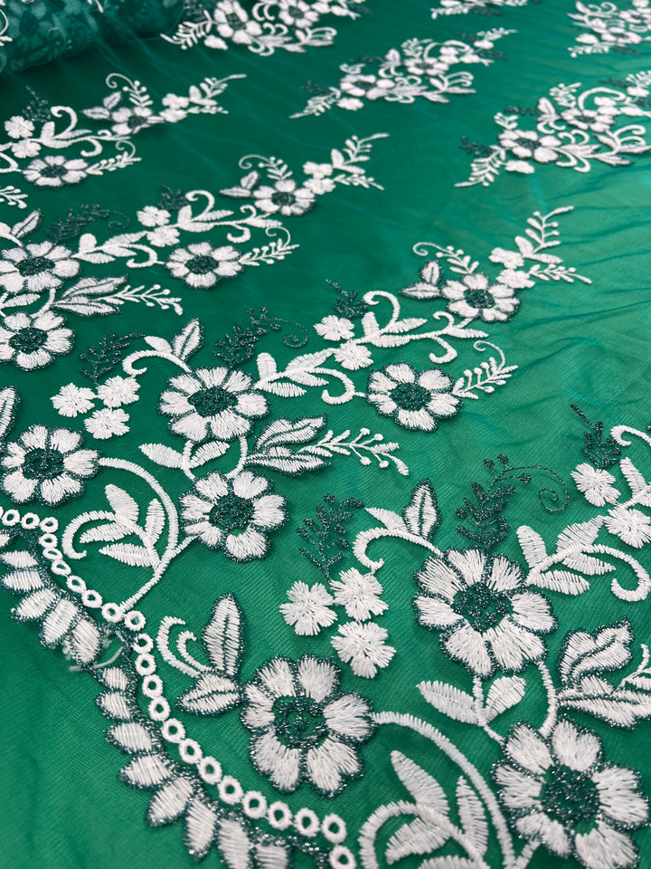 Close-up of a section of Embroidered Lace - Teal - 150cm by Super Cheap Fabrics, featuring detailed white floral embroidery. The design showcases an array of flowers, leaves, and branches arranged in a repeating pattern, highlighting the intricate stitching and craftsmanship on the lightweight fabric.