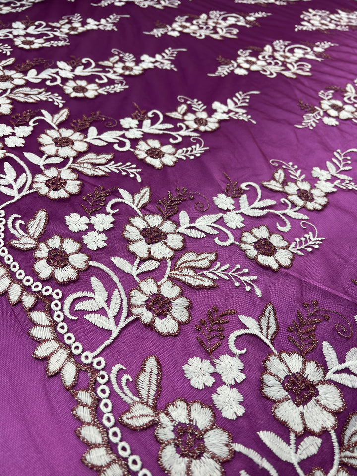 A close-up of the intricate floral and leaf embroidery in white and gold thread on the rich plum-colored, lightweight fabric from Super Cheap Fabrics. The delicate patterns on this Embroidered Lace - Plum - 150cm feature a combination of detailed flowers, leaves, and decorative swirls, creating an elegant and ornate design reminiscent of fine lace.