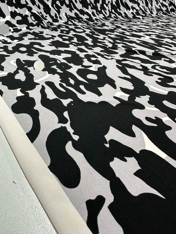 A close-up image showcasing the medium-weight Printed Lycra - Camo by Super Cheap Fabrics, featuring an intricate black and white camouflage pattern. The 150cm wide Polyester/Spandex fabric is laid out flat, emphasizing its detailed and contrasting design.