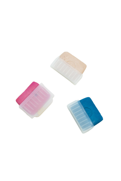 Three rectangular tablets of Super Cheap Fabrics tailor's chalk in pink, blue, and white rest on a white surface. Each vibrant piece is partially housed in its own clear, textured holder, beautifully showcasing the upper part of the chalk and highlighting all three colors.