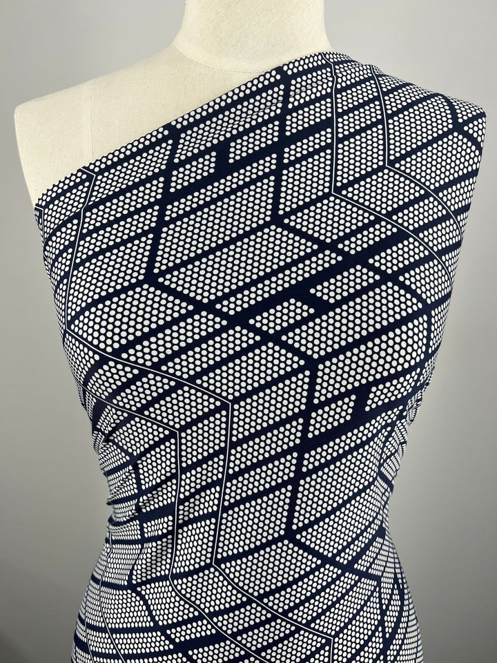 A mannequin dressed in a one-shoulder garment made from Super Cheap Fabrics' Printed Lycra - Grid - 150cm, a medium-weight Polyester/Spandex fabric featuring a navy blue and white geometric pattern with intricate dots and lines that create a visually striking and modern look against the white background.