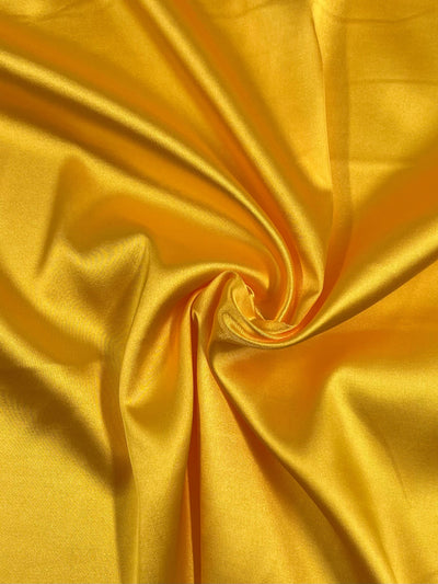 A close-up view of the Satin Deluxe - Yellow - 150cm by Super Cheap Fabrics reveals crumpled material with a smooth, shiny finish that reflects light, accentuating its luxurious texture. The folds and creases create dynamic patterns and depth in this lightweight fabric.