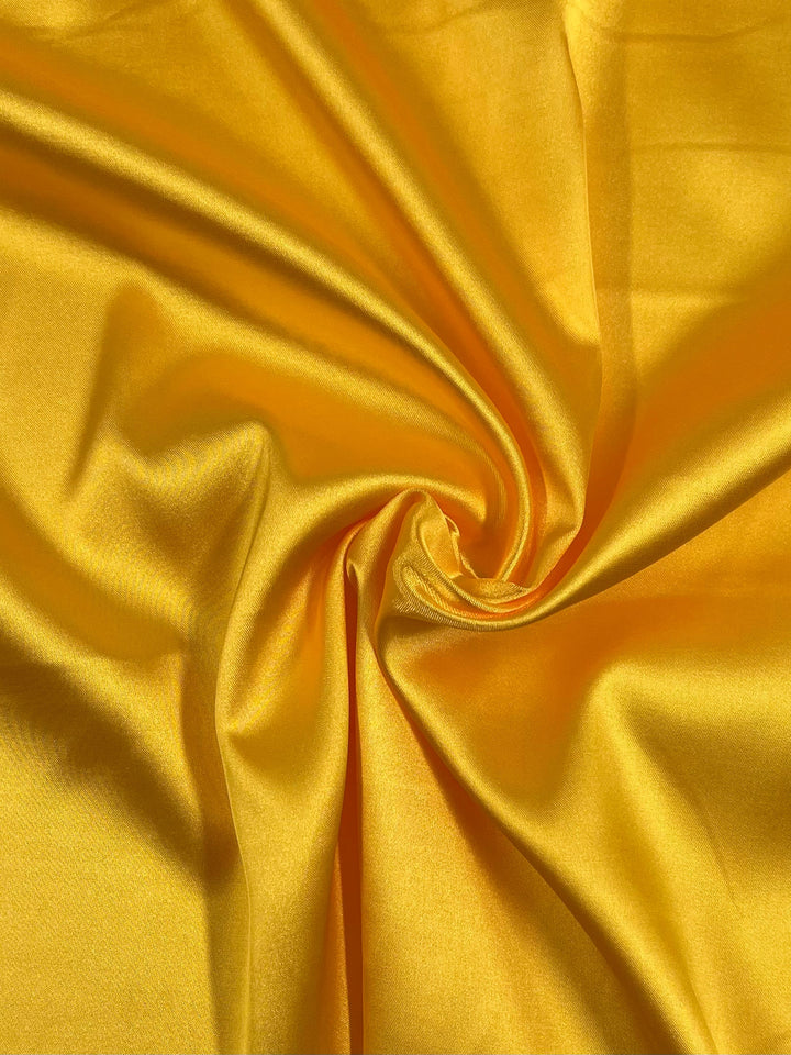A close-up view of the Satin Deluxe - Yellow - 150cm by Super Cheap Fabrics reveals crumpled material with a smooth, shiny finish that reflects light, accentuating its luxurious texture. The folds and creases create dynamic patterns and depth in this lightweight fabric.